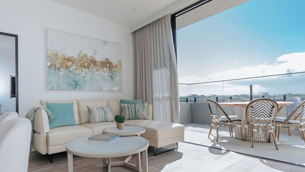 A modern living room with a sofa set, a round coffee table, and a dining area with wicker chairs.