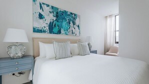 A hotel room with a large bed, two bedside tables, a large abstract painting, and a window with curtains.