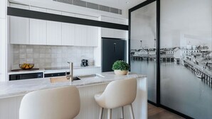 A modern kitchen with white cabinetry, a marble countertop, and two bar stools.