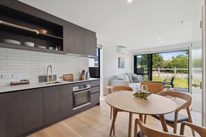 A modern kitchen with dark cabinetry, white subway tiles, and a wooden dining table with chairs. - Ruru Retreat (Wanaka)