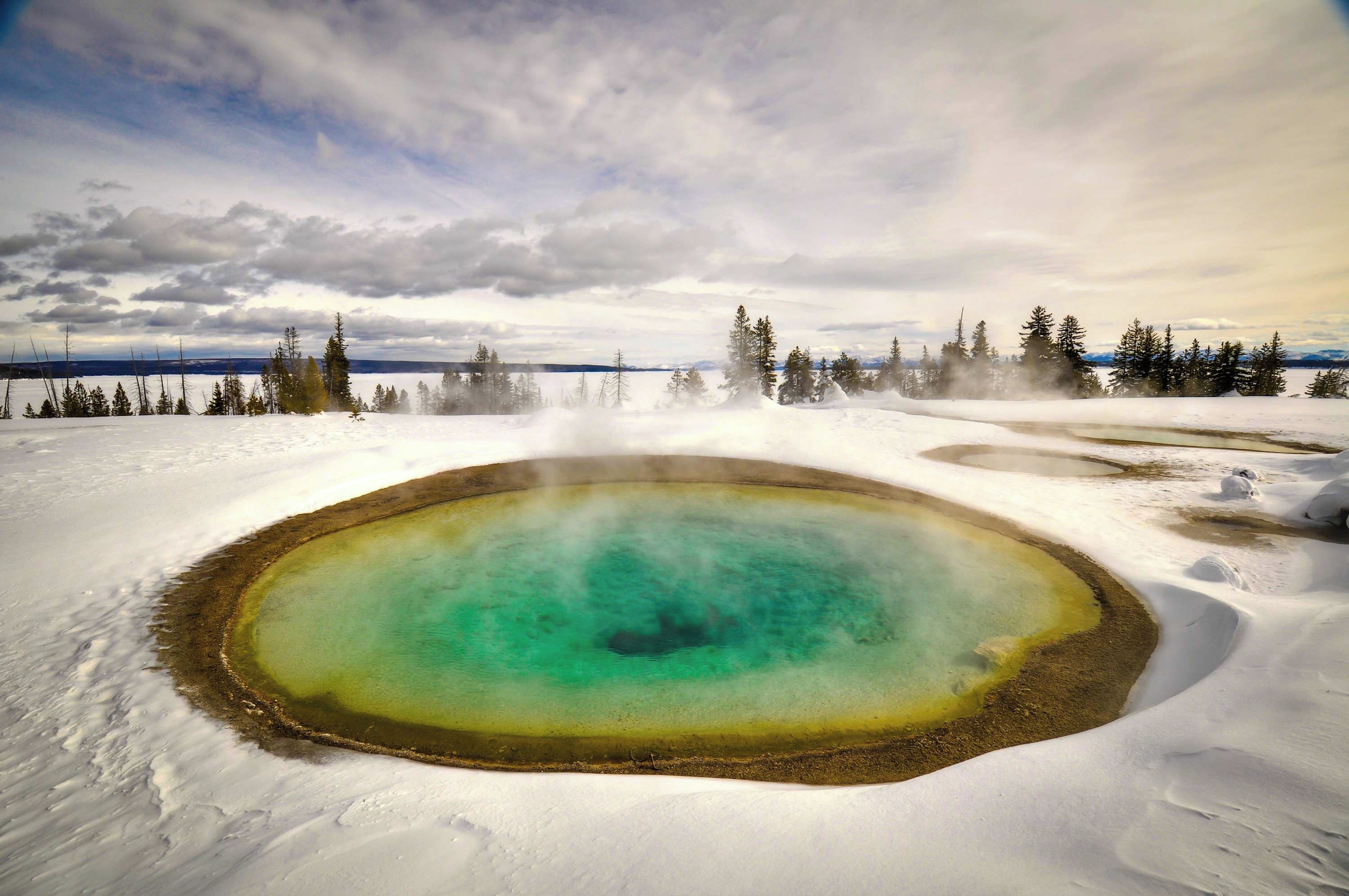 Ein geothermal beheiztes Thermalbad, umgeben von Schnee und Bäumen.