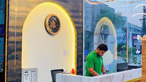 A modern hotel reception desk with a marble counter, wooden paneling, and a large mirror reflecting the interior. - Hotel Pravasa Stay, Dewas Naka (Indore)
