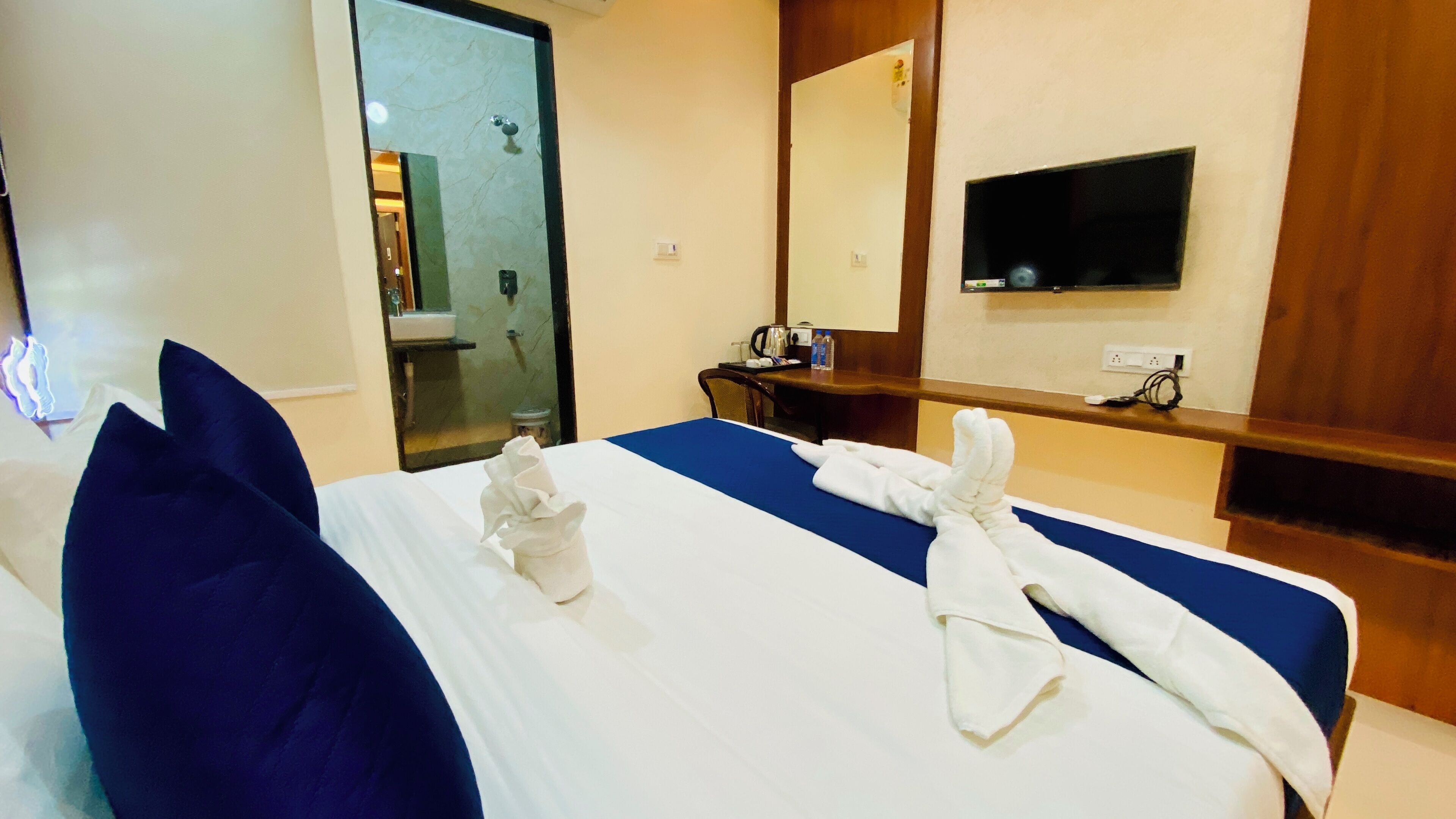 A hotel room with a bed, a desk, a mirror, and a TV.