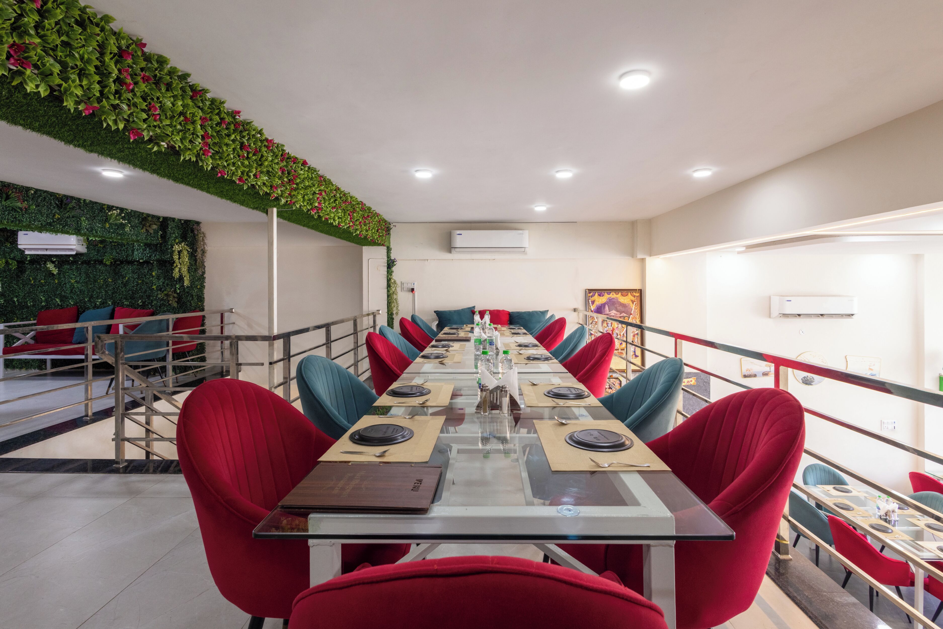 A conference room with a long table, red chairs, and a green wall with plants.
