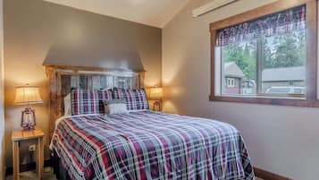 A bedroom with a bed, two bedside lamps, a window with a view, and a plaid bedspread.