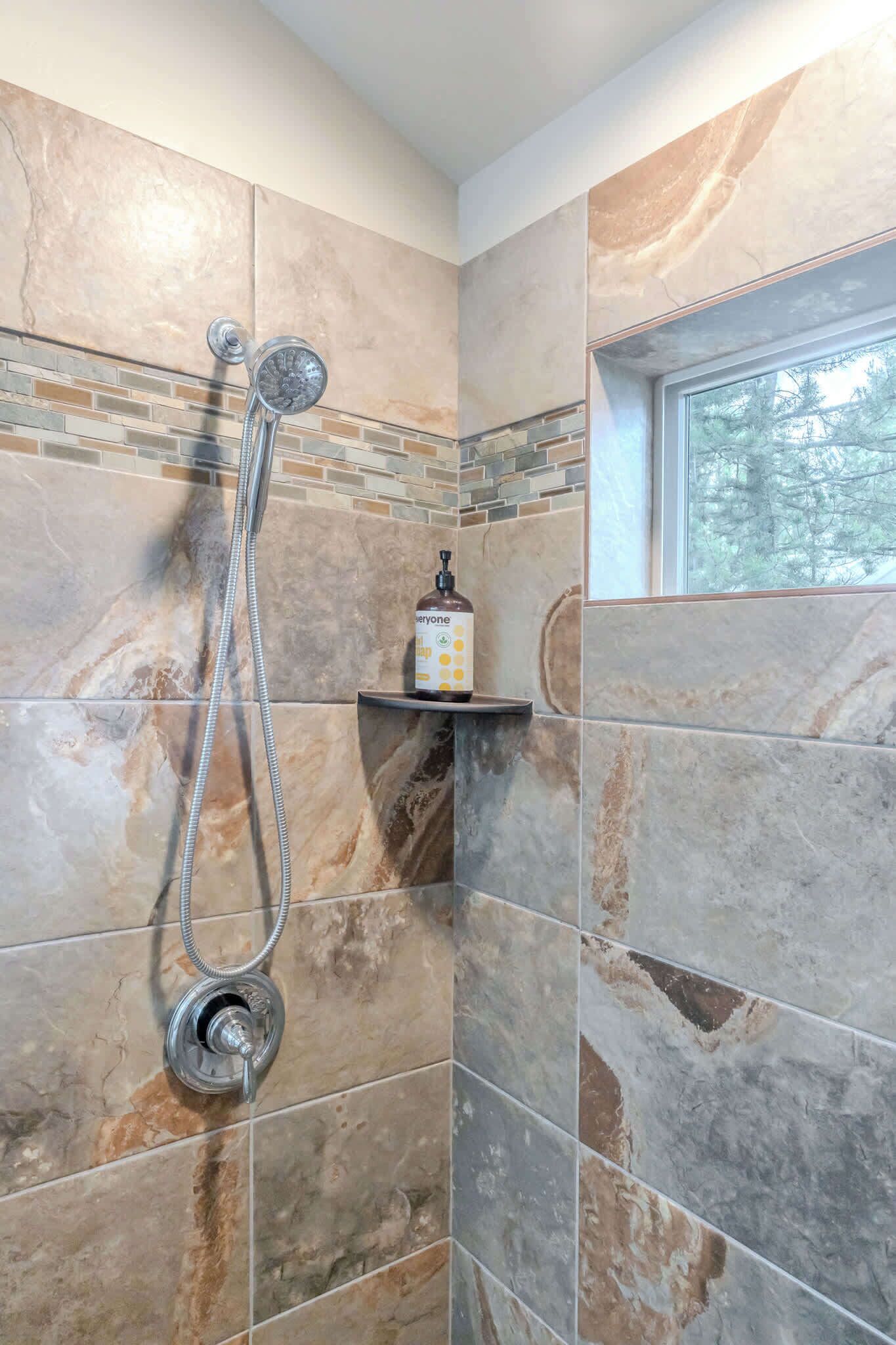 A shower area with a handheld showerhead and a bottle of soap on a shelf.