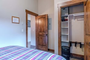 A bedroom with a bed, a wooden door, a closet with hanging items, and a wall-mounted light switch. - Montana Cabin Summary (West Yellowstone)