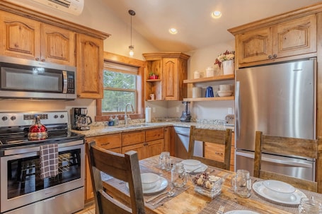 A modern kitchen with wooden cabinets, stainless steel appliances, and a dining area set for four.