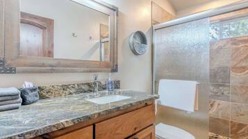 A bathroom with a granite countertop, a sink, a mirror, a towel rack, and a shower enclosure.
