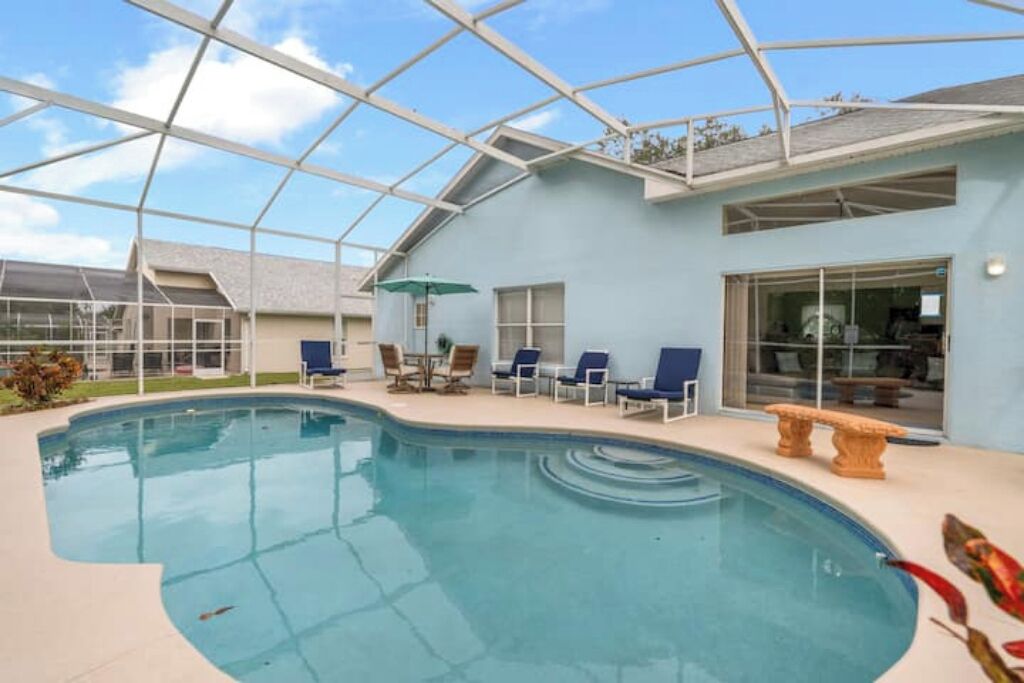 A pool area with a glass enclosure, lounge chairs, and a table.