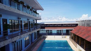 A swimming pool with a view of a building with balconies and a red-roofed structure. - Hidden Valley Beach Resort (Pinamungajan)