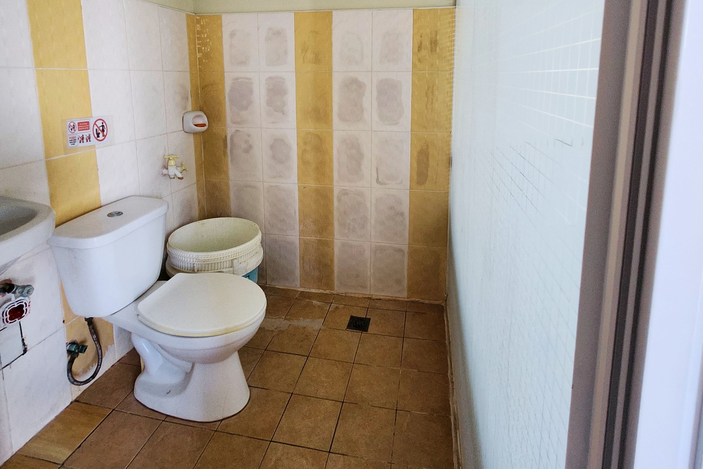 Een kleine badkamer met toilet, bidet en handdroger. Er is een bord aan de muur en een betegelde vloer.