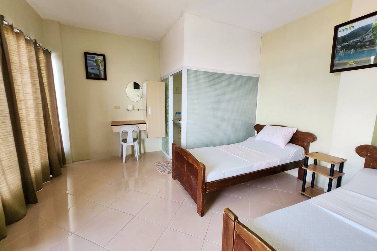 A hotel room with a bed, a desk, a chair, a mirror, and a window with curtains.