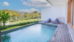 A modern outdoor pool area with a wooden deck, a seating area with cushions, and a view of a lush green landscape. - Villa Taman Famindo Canggu V-8 (Canggu)