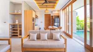 A modern living room with a sofa, wooden furniture, and a view of a swimming pool. - Villa Taman Famindo Canggu V-8 (Canggu)