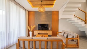 A modern living room with a wooden sofa, a TV, and a staircase. - Villa Taman Famindo Canggu V-8 (Canggu)