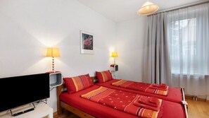 Habitación de hotel con cama, dos lámparas de noche, un televisor y una ventana con cortinas.