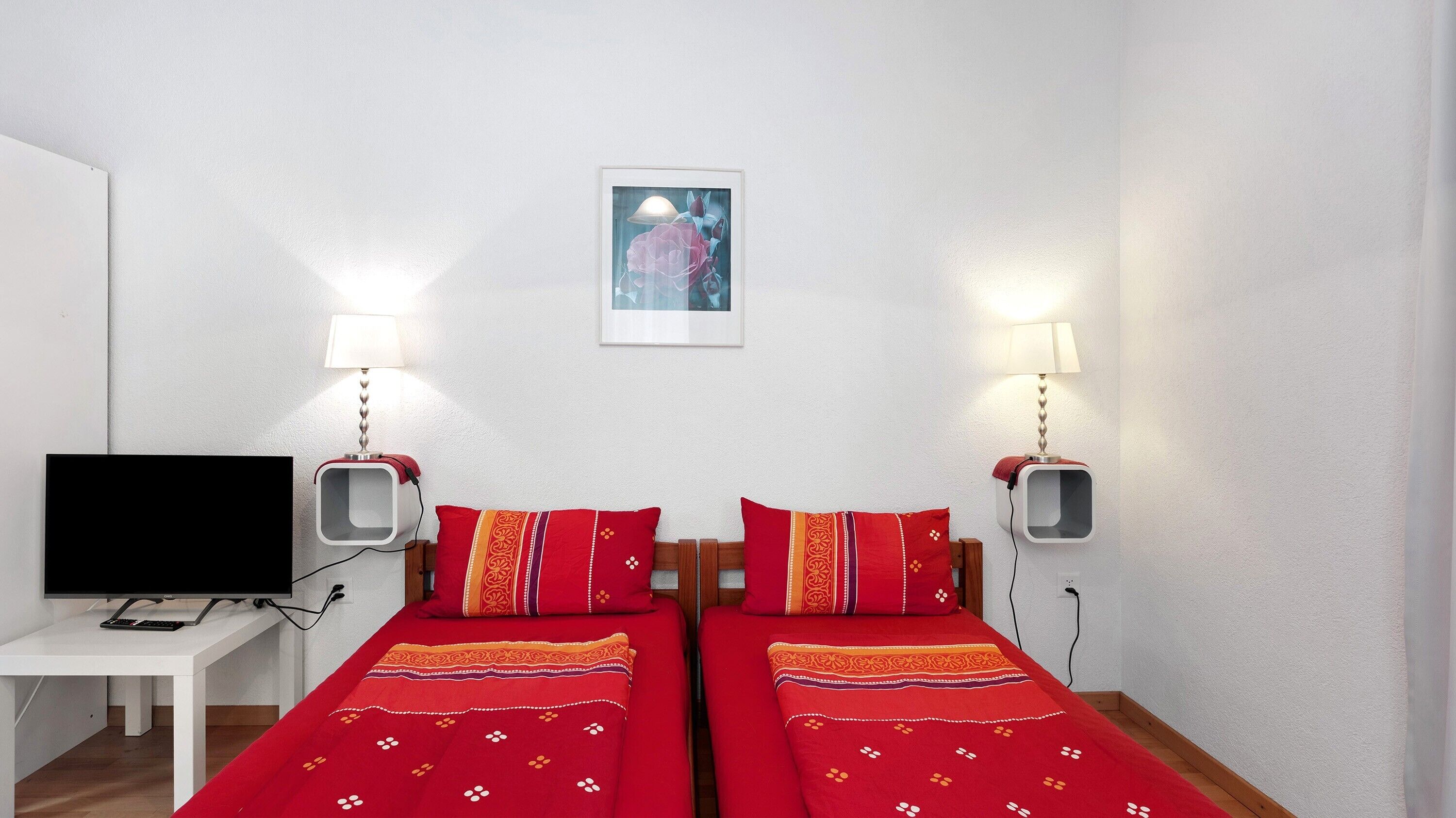 Ein Zimmer mit zwei Betten, einem Fernseher und zwei Wandleuchten.