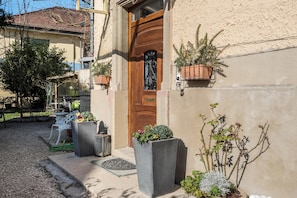 Un edificio con puerta de madera, plantas en macetas y una silla blanca en el exterior.