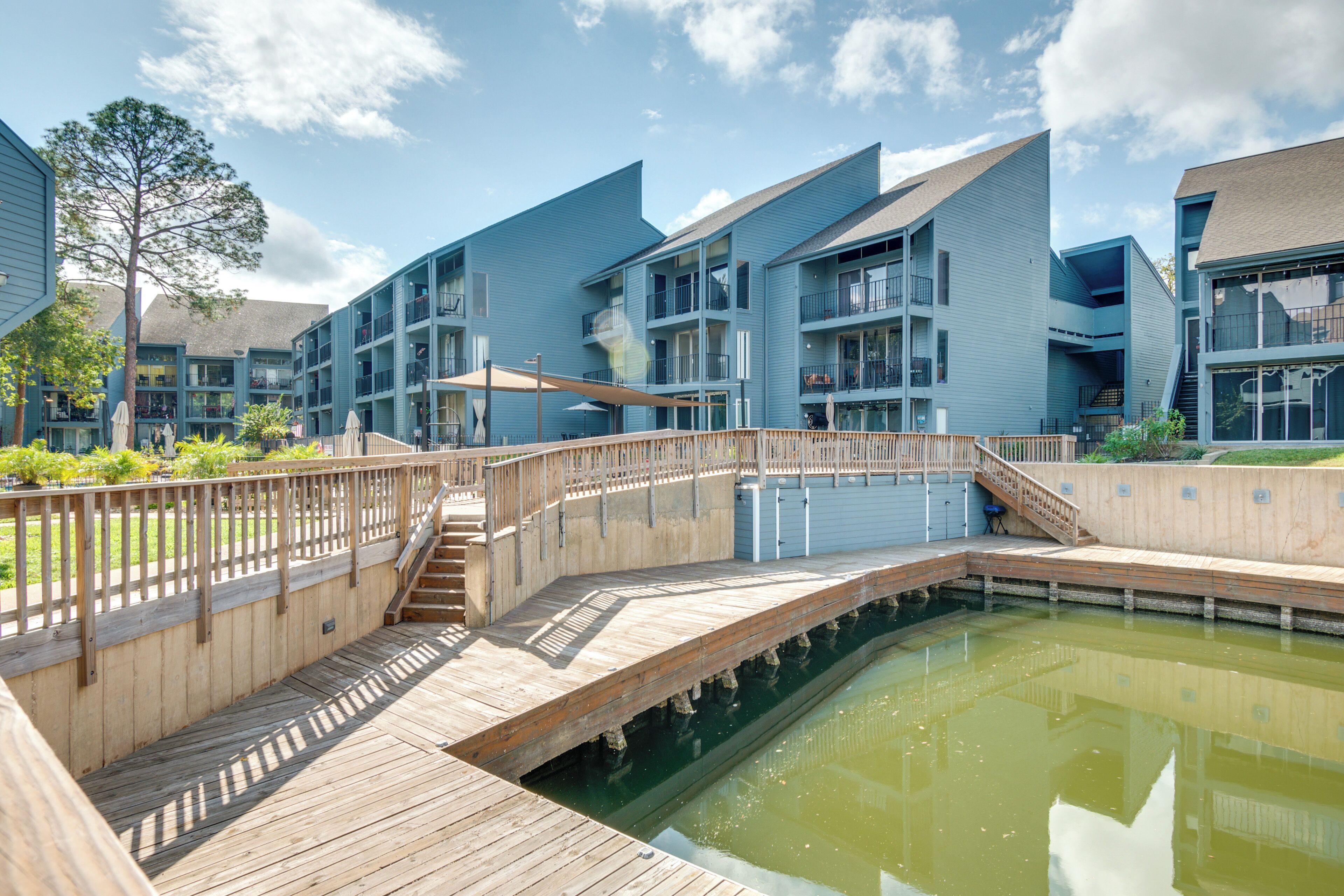 A modern building with multiple balconies and a wooden deck over a pond.