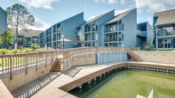 A modern building with multiple balconies and a wooden deck over a pond.