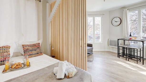 A hotel room with a bed, breakfast tray, breakfast, a sofa, a dining table, chairs, a clock, and a window. - Mark 22 - Large studio Canal Saint-Martin views (Paris)