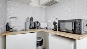 A compact kitchen with white tiled walls, a stainless steel sink, a coffee maker, a kettle, and a microwave. - Mark 22 - Large studio Canal Saint-Martin views (Paris)