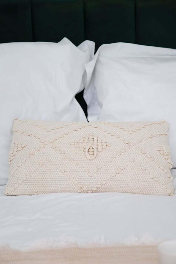 A bed with white linens and a decorative pillow with a textured pattern.
