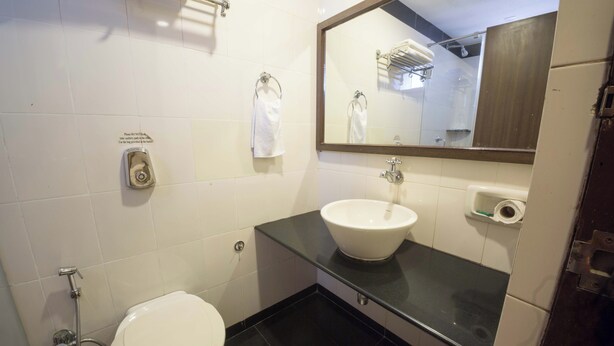 A bathroom with a toilet, sink, mirror, towel rack, and a trash bin. - Hotel Aroma Executive (Panaji)