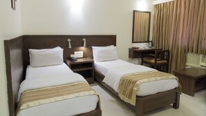 A hotel room with two single beds, a desk, a chair, a mirror, and a window with curtains. - Hotel Aroma Executive (Panaji)