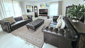 A living room with a large sectional sofa, a coffee table, a TV, and a large plant. - Portmarnock House (Cape Town)