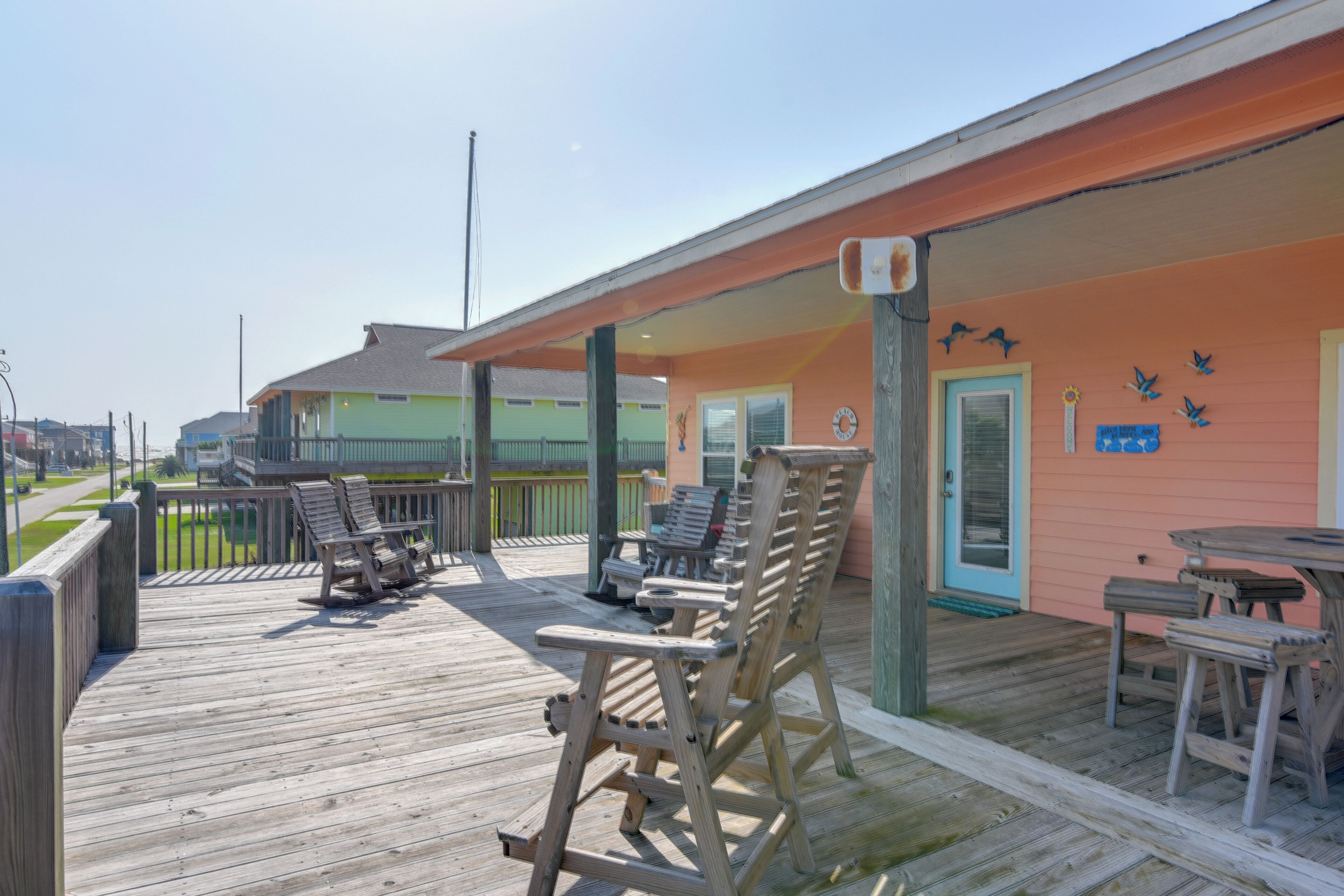 Een houten terras met buitenmeubels en een gebouw met een perzikkleurige gevel.