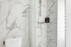 Experience a luxurious bathroom with a sleek design, featuring a chrome showerhead and handheld attachment, and a well-appointed space for toiletries.