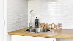 A modern kitchen with a stainless steel sink, a soap dispenser, and a wooden 'Welcome Home' sign. - TBS 23 - Pretty suite in Canal Saint-Martin area (Paris)