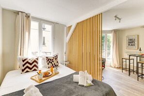 A hotel room with a bed, breakfast tray, towels, and a view of the outside.