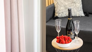 A room with a grey sofa, a patterned pillow, a bottle of wine, two glasses, and a bowl of strawberries on a small round table. - TBS 23 - Pretty suite in Canal Saint-Martin area (Paris)