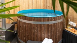 A wooden hot tub with a blue interior, a black bench, and a bottle of wine and glasses on a wooden table. - Tropical Wellness Suite Sauna, whirlpool, TV, BBQ (Büdesheim)