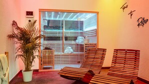 A spa room with wooden loungers, a potted plant, and a glass door leading to a sauna area. - Tropical Wellness Suite Sauna, whirlpool, TV, BBQ (Büdesheim)