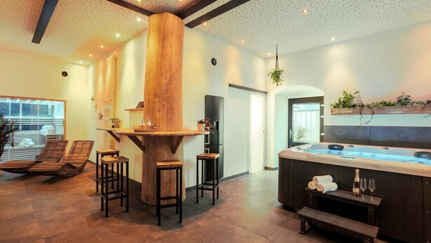 A modern spa room with a wooden bar, seating area, and a hot tub. - Tropical Wellness Suite Sauna, whirlpool, TV, BBQ (Büdesheim)