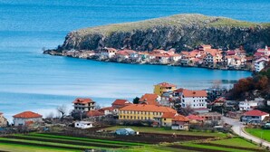 Une ville côtière avec des bâtiments le long du littoral, une colline imposante et des champs agricoles.