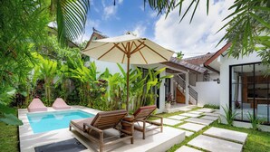 A modern outdoor pool area with lounge chairs and a large umbrella, surrounded by lush greenery and a well-maintained garden. - Milla Villa by Betterplace (Ubud)