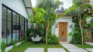 A modern house with a glass door, a wooden door, and a garden with a swing chair, concrete steps, and various plants. - Milla Villa by DH (Ubud)