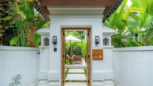 A white-walled entrance with a wooden door leading to a covered outdoor seating area. - Milla Villa by Betterplace (Ubud)