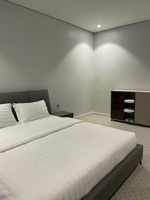 A modern hotel room with a large bed, a nightstand, a wardrobe, and a small desk. - Qimam Park 5 Abha (Abha)