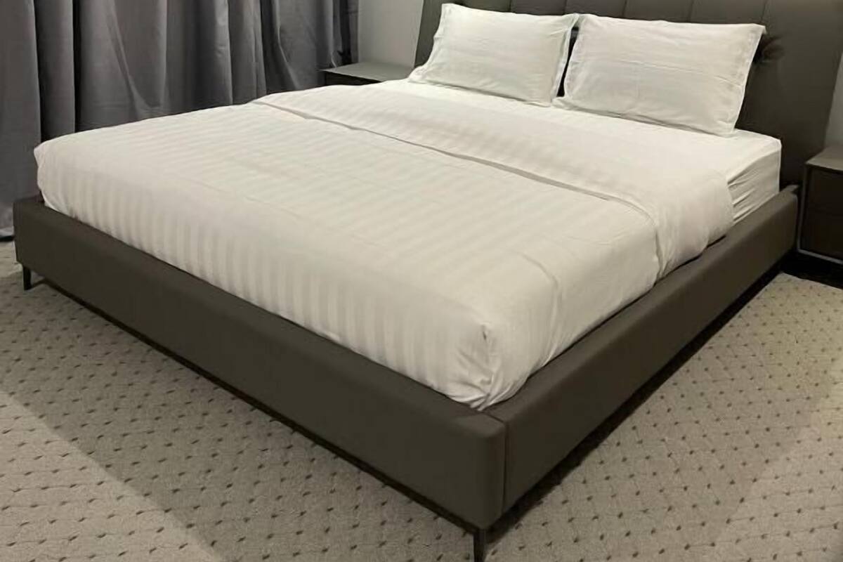 A modern bedroom with a large bed, grey curtains, and a simple nightstand.
