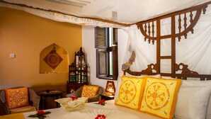 A traditional room with a bed, a small table, and a chair. - Coconut romantic Double Room (Jambiani)