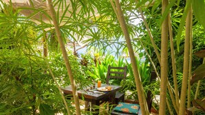 A table set outdoors surrounded by lush greenery, with a chair and a small table.