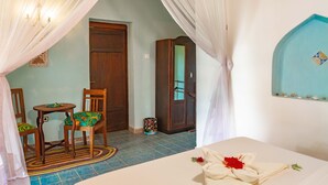 A room with a bed, a chair, a small table, a mirror, and a door. - Crystal Blue - Comfort Double Room Sea View with AC (Jambiani)