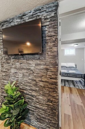 Una habitación con pared de piedra, televisor de pantalla plana montado y una planta en maceta.