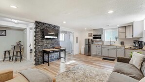 Un salon moderne avec un mur d’accent en pierre, un téléviseur à écran plat, une cuisine équipée d’appareils électroménagers en acier inoxydable et un coin salon confortable.